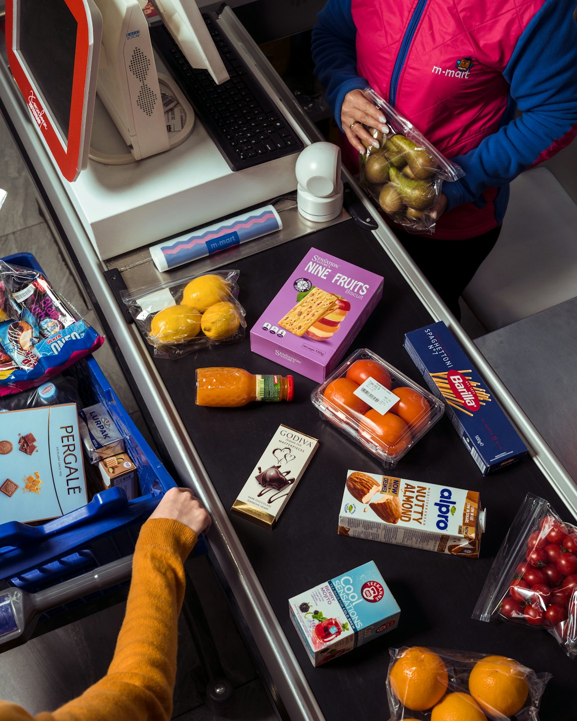 Customer places groceries on supermarket checkout conveyor belt.