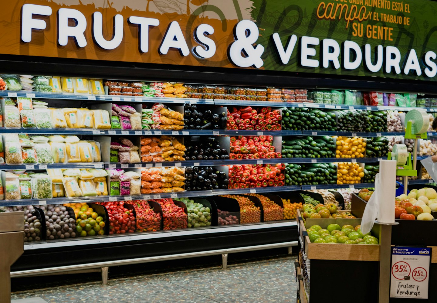 Supermarket aisle displays fresh fruits and vegetables for sale.