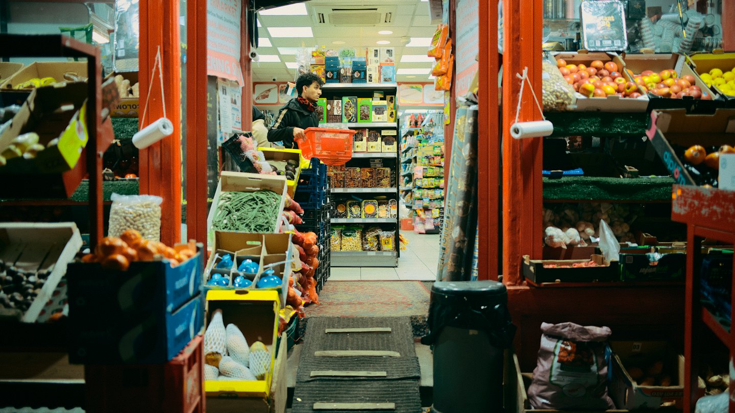 Man with red basket shops in a busy grocery store aisle.